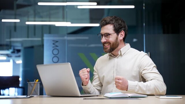 Happy excited businessman sitting at workplace in office celebrating success. Smiling entrepreneur reading great news on laptop, feeling surprised, thrilled after receiving positive business message