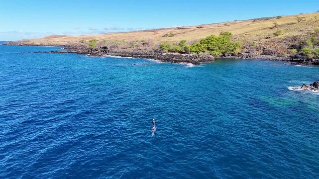 Aerial view of a person hydrofoil surfing over the clear, blue ocean waters under a bright sky, creating a mesmerizing scene, Hawi, Hawaii, United States.