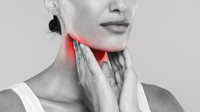 Closeup of sick lady having sore throat, touching her neck with red inflamed zone, suffering from laryngeal disorder, tonsillitis, throat cancer, cold, black and white gray studio background, banner