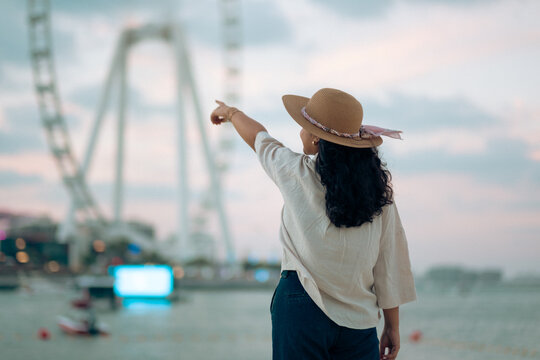 Woman pointing at Dubai Ain observation wheel while enjoying waterfront lifestyle at sunset, Dubai Marina, JBR, ocean views