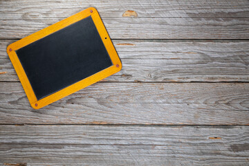 Top-down view of a small blank vintage chalkboard with wooden frame slightly tilted in the top-left corner on a rustic gray wooden table
