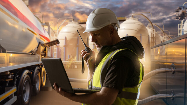 Energy logistics, Fuel terminal operations. Engineer uses radio and laptop near tanker and storage tanks, shipment coordination and safety monitoring.