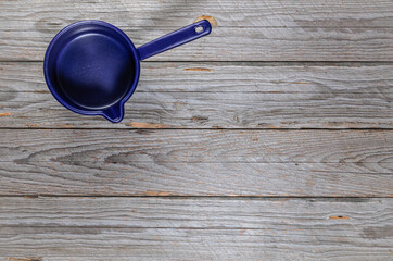 Top-down view of a small empty enamel pot with handle and spout in blue-purple tones on a rustic gray wooden table
