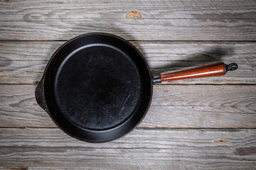 Top-down view of a large empty cast iron skillet with wooden handle on a rustic gray wooden table
