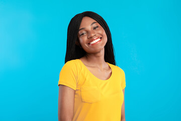 Fototapeta premium Cheerful Black Woman With Braided Cornrows Hairstyle Smiling To Camera Posing Standing Over Blue Background. Studio Portrait Of Pretty African American Young Lady With Toothy Smile Concept
