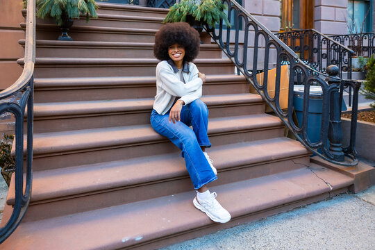 Smiling woman sitting on brownstone stoop enjoying city life