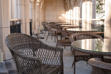 Naklejka premium Patio Wicker Chairs Tables Restaurant - A row of wicker chairs and tables on a patio outside a restaurant.