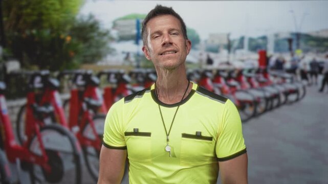 Man with arms crossed, whistle on a lanyard and neon shirt at bike rental parking on a city street; confidence urban service.
