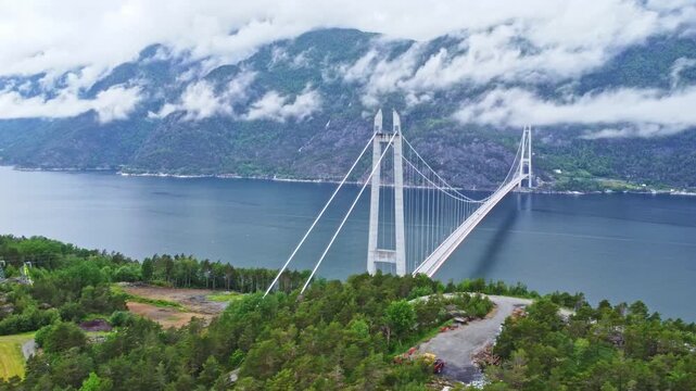 Aerial view of the Hardangerbrua bridge spanning across the serene waters, nestled between lush green hills and cloudy skies, Bergen, Vestland, Norway.