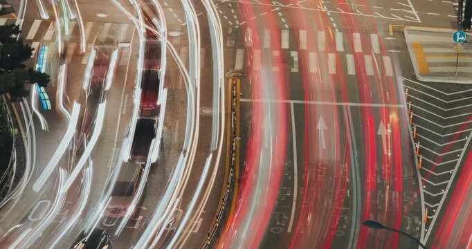 Time-lapse. Vehicles navigate a bustling intersection under night lights, capturing the continuous movement and energy of urban traffic with illuminated road markings and signals