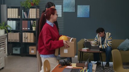 Tracking shot of adult Caucasian manager gesturing toward workspace while welcoming female newcomer holding cardboard box with personal items in modern office