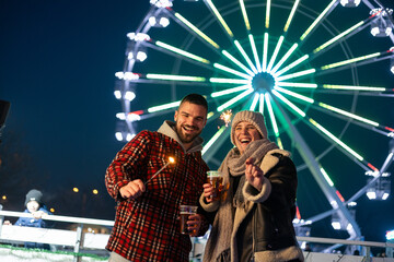 Couple celebrating holiday season at fairground with sparklers