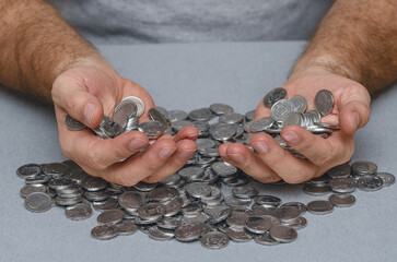 Male hands holding coins slipping through fingers on gray background. False expectations about money