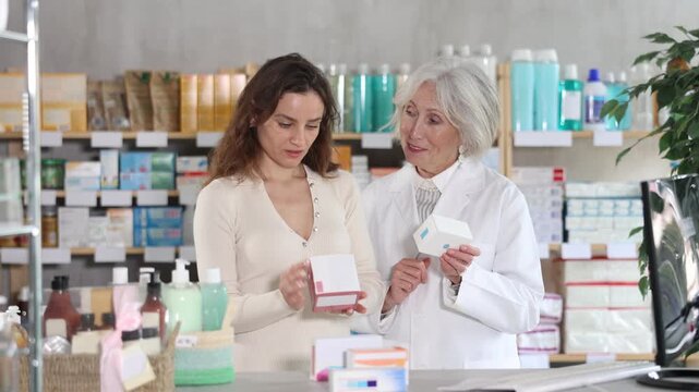 Female client purchases pills to treat chronic disease. Senior woman pharmacist in background offers product, promotes product of European brand, recommend safe and effective pills.