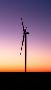 View of a lone wind turbine stands as a dark sentinel against the vibrant canvas of a sunset sky, blending orange, pink, and purple hues, Liw, Masovian Voivodeship, Poland.