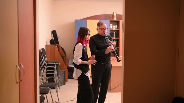 A teenage girl with pink hair, an informal girl, learns to play the clarinet at a music school, a music lesson with a teacher