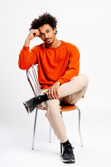 Confident young man with curly hair posing in orange sweatshirt and khaki pants