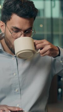 Arabian businessman creative Indian business man writing notes ideas drinking tea coffee in cafe working distant male guy executive specialist noting work plan write in notebook enjoying beverage