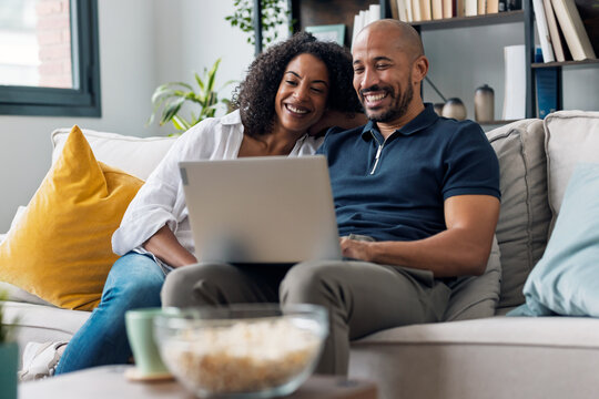 Happy beautiful couple using computer while sitting on the couch at home.