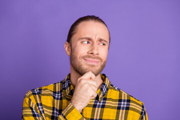 Young handsome man in checkered yellow plaid shirt posing thoughtfully against purple background