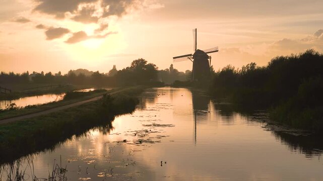 Sunrise on the Dutch iconic landscape with a windmill, canal and dike