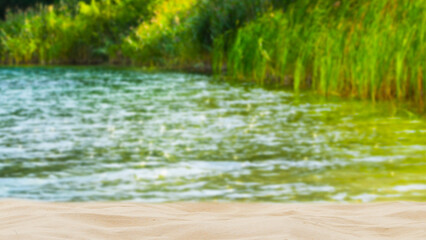 idyllic sand beach and reeds lakeside in sommertime, blurred background with copy space in foreground for product presentations, sunny backdrop for beauty spa, vacation, travel and relaxation