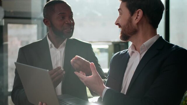 Two multiracial business men team with laptop partnership businessmen working together in office Caucasian man talking to African American male workmates discuss sales happy agree startup idea success