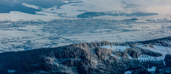 Winter cityscape of Miercurea Ciuc during the blue hour, with forest and Kossuth Rock in the foreground, extreme cold, Harghita County, Romania.