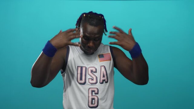 Man in usa basketball jersey gesturing with hands in studio against turquoise backdrop; playful confidence.