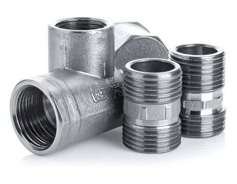 Close-up of shiny metal plumbing fittings against a white backdrop, including a T-joint, two threaded connectors