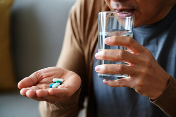 Impotence and physical weakness Man holding pills in hand drinking water from glass