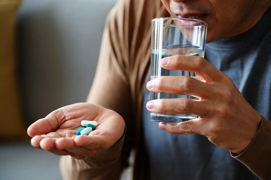 Impotence and physical weakness Man holding pills in hand drinking water from glass