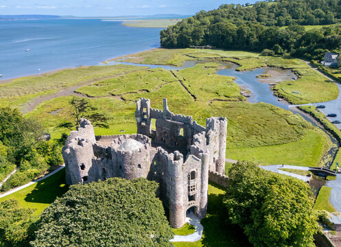 Aerial view of the majestic ruins of Laugharne Castle stand proudly against the backdrop of green marshland and the glistening Taf Estuary, Carmarthen, Wales, United Kingdom.