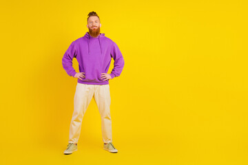 Young man in purple hoodie stands with hands on hips against yellow background showcasing casual...