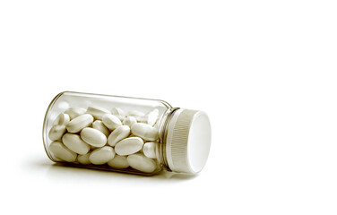 White Pill Bottle filled with white ovel shaped Pills laying on a white background