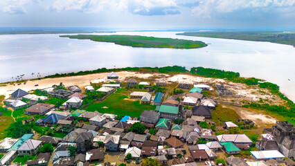 Aerial view of houses clustered densely near the riverbank, with a lush island visible in the distance, Andoni, Rivers State, Nigeria.