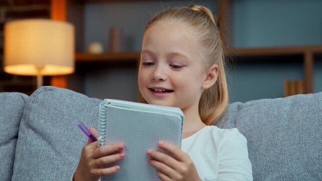 Caucasian girl child kid daughter reading text in copybook read in notebook at home studying distant remote education learning primary schoolgirl preparing homework notes study learn in living room