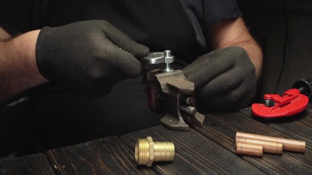 A skilled technician tightens metal nuts with a wrench in a vise during a detailed repair