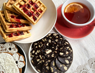 Still life with Belgian waffles, chocolate sausage dessert, gingerbread and a cup of tea.