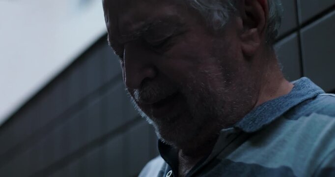 Elderly man close up with eyes closed leaning against wall expressing deep emotional struggle inner silence despair and psychological pain during prolonged hardship