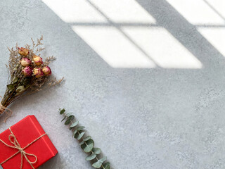 Red gift box and dried flowers with window shadows, text space. Top view