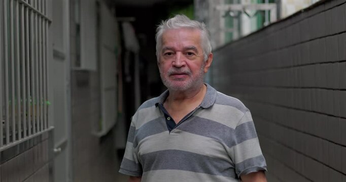 Elderly man outdoors standing in narrow passage looking at camera with calm thoughtful expression conveying life experience resilience maturity and quiet confidence