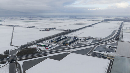 Aerial view of a stark white winter landscape with a modern industrial complex, the dark structures contrasting against the snow-covered fields, Datacenter, Noord-Holland, Netherlands.