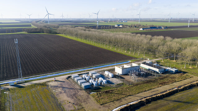 Aerial view of wind turbines standing tall against the horizon, bordered by dark, tilled fields and a line of bare trees, Almere, Netherlands.