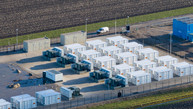 Dronten, Netherlands - 14 January 2026: Aerial view of rows of white energy storage containers casting long shadows on the gravel amidst agricultural fields.