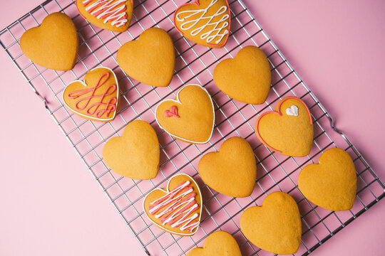 Sweet homemade Valentine's Day heart shaped cookies with white and pink icing on a pink background