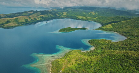 Islands covered with lush green rainforests surrounding a tranquil turquoise bay, featuring shallow coral reefs reflecting clear waters and an overcast sky