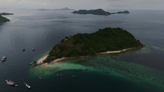 Drone footage of Pulau Kelor in Komodo National Park, Indonesia, showing a small tropical island with white sand beach, green vegetation and clear turquoise water in calm conditions, captured in 4K.