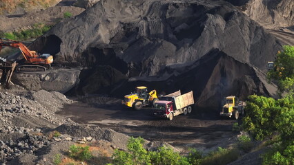 Large open-pit quarry with massive excavators and dump trucks loading and hauling coal and ore, showing heavy machinery, earthmoving operations and dusty industrial landscape