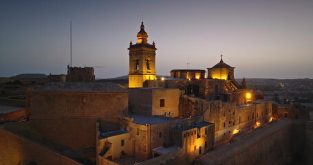 Malta, Comino island: Cittadella in Gozo at night, illuminating by warm lights create a captivating sunset scene that highlights historic architecture and travel destination. Drone flight